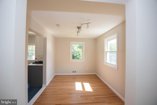 unfurnished dining area featuring rail lighting, light wood-style floors, baseboards, and visible vents