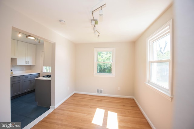 unfurnished dining area with visible vents, baseboards, rail lighting, and light wood-style floors