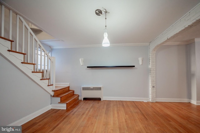 unfurnished living room featuring radiator heating unit, wood finished floors, stairway, baseboards, and ornamental molding