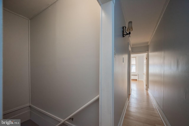 hallway featuring light wood finished floors, radiator heating unit, baseboards, and crown molding