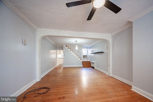 unfurnished living room featuring a ceiling fan, light wood-style flooring, stairs, a textured ceiling, and crown molding