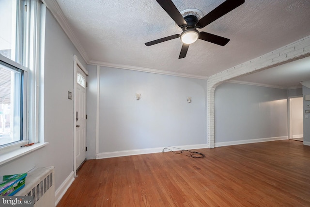 spare room with a textured ceiling, wood finished floors, ceiling fan, plenty of natural light, and baseboards