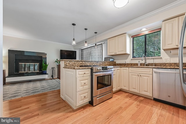 kitchen featuring light wood-style floors, ornamental molding, cream cabinetry, a sink, and stainless steel appliances