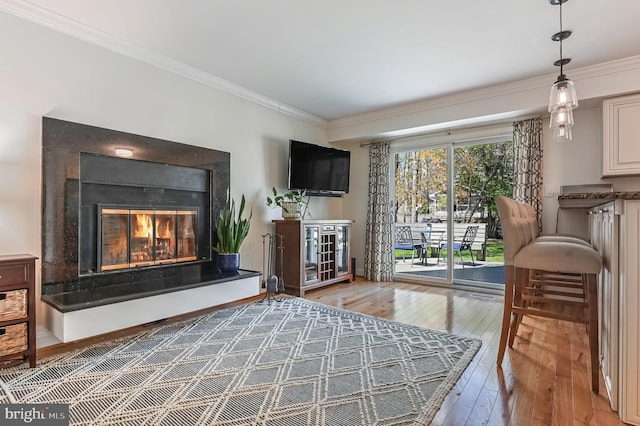 living area with hardwood / wood-style floors, ornamental molding, and a glass covered fireplace