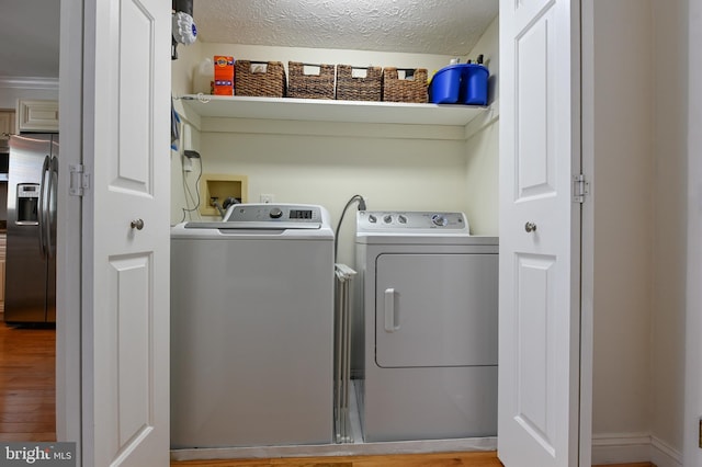 clothes washing area with laundry area, wood finished floors, washing machine and dryer, and a textured ceiling