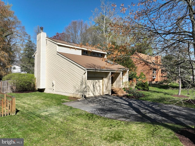 back of house with aphalt driveway, a yard, fence, a chimney, and a shingled roof