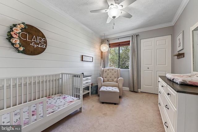 bedroom featuring a textured ceiling, light colored carpet, ornamental molding, and a nursery area