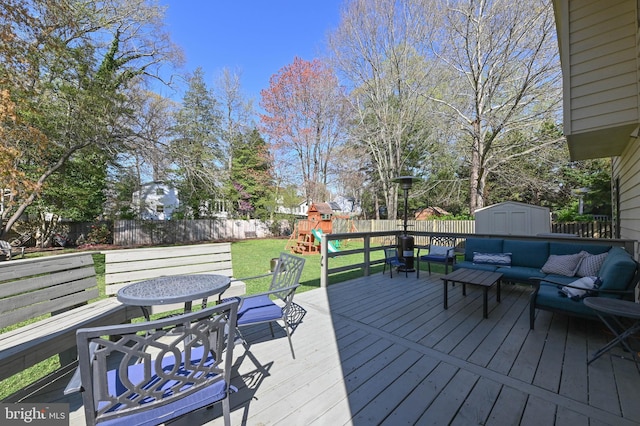 deck with an outdoor living space, an outbuilding, a storage shed, a fenced backyard, and a playground