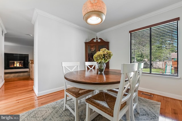 dining area with crown molding, light wood-style flooring, a glass covered fireplace, visible vents, and baseboards