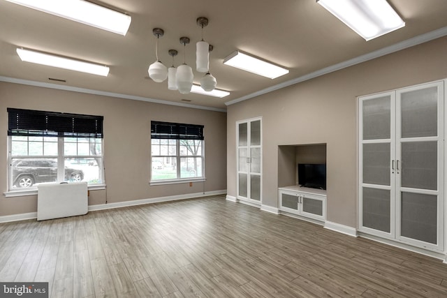 unfurnished living room with baseboards, wood finished floors, an inviting chandelier, and ornamental molding