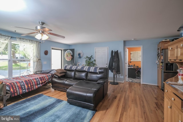 living room with baseboards, a ceiling fan, and light wood finished floors