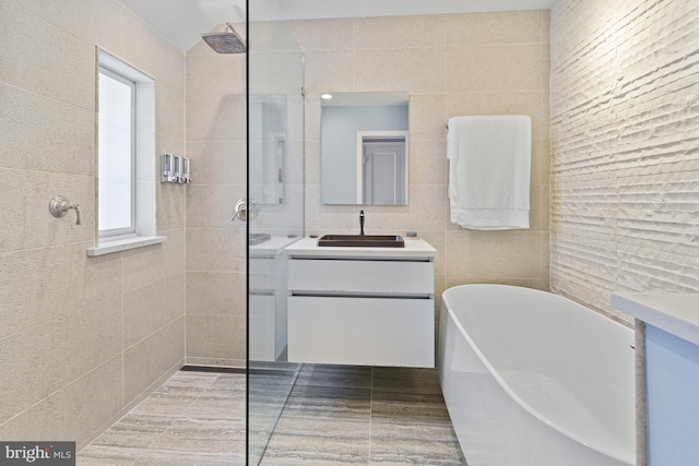 bathroom featuring a freestanding bath, vanity, a walk in shower, and tile walls