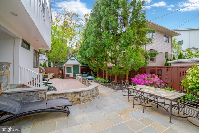 view of patio featuring a fenced backyard, a storage shed, outdoor dining space, a wooden deck, and an outbuilding