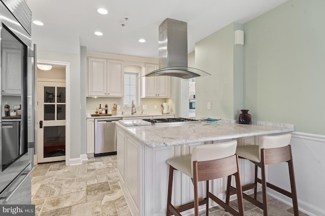 kitchen featuring island exhaust hood, a breakfast bar, dishwasher, a peninsula, and gas stovetop
