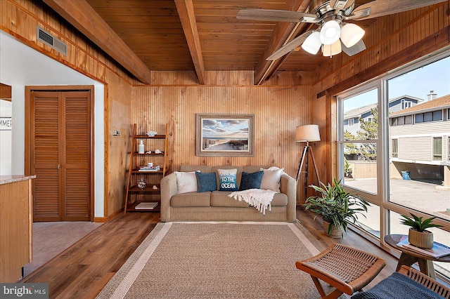 living area with wooden walls, visible vents, beam ceiling, wooden ceiling, and wood finished floors