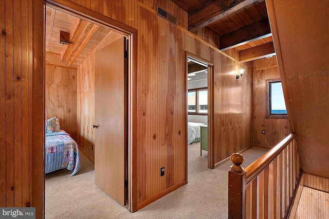 hall featuring wooden walls, beamed ceiling, carpet flooring, and visible vents