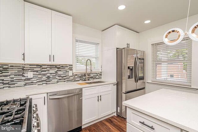 kitchen with appliances with stainless steel finishes, a sink, light countertops, white cabinetry, and backsplash