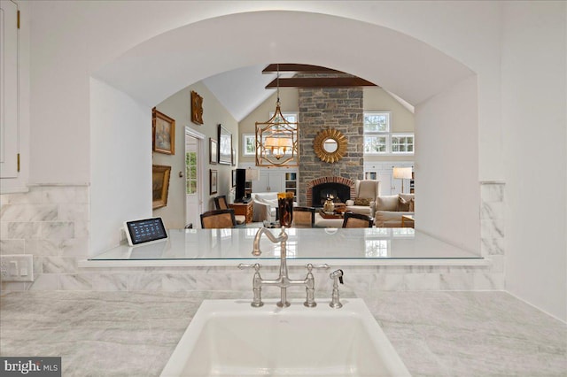 kitchen featuring arched walkways, a sink, light countertops, a stone fireplace, and vaulted ceiling