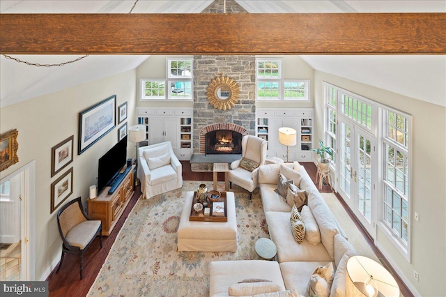 living area featuring a wealth of natural light, a stone fireplace, vaulted ceiling with beams, and wood finished floors