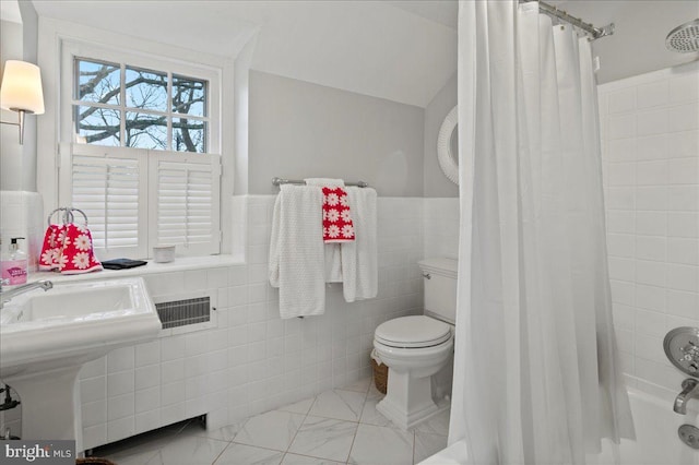 bathroom featuring marble finish floor, shower / tub combo with curtain, toilet, wainscoting, and tile walls