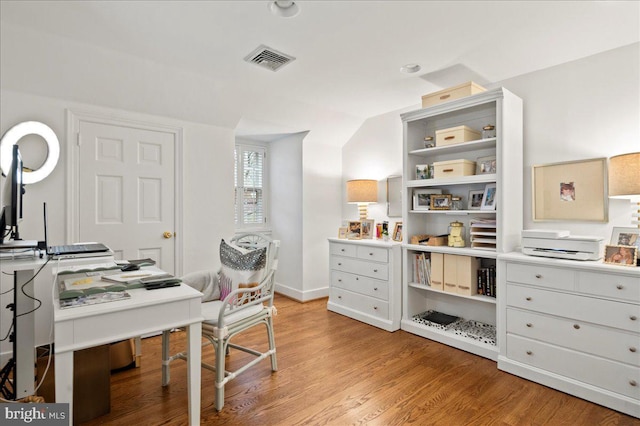 office space with visible vents, baseboards, light wood finished floors, and vaulted ceiling