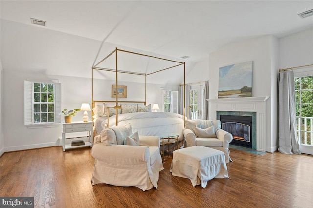 bedroom with wood finished floors, a high end fireplace, vaulted ceiling, and visible vents