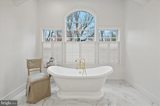 bathroom with a soaking tub, marble finish floor, and baseboards