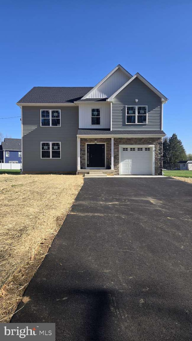 view of front of house featuring an attached garage, stone siding, and aphalt driveway