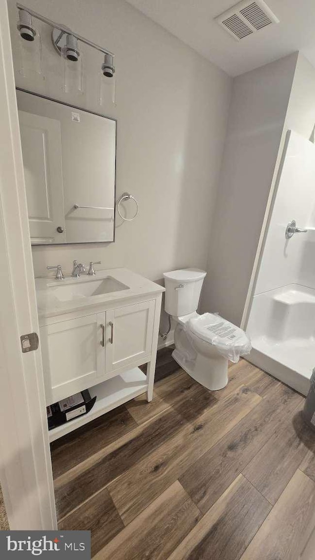full bathroom featuring vanity, toilet, a shower stall, visible vents, and wood finished floors