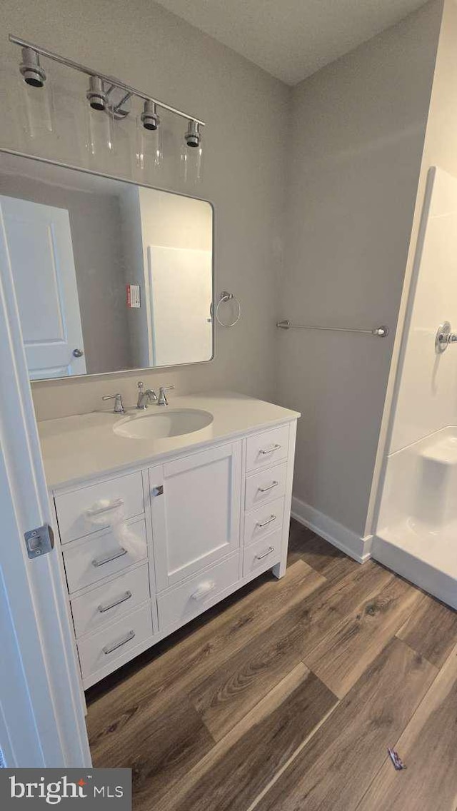 full bath featuring vanity, baseboards, walk in shower, and wood finished floors