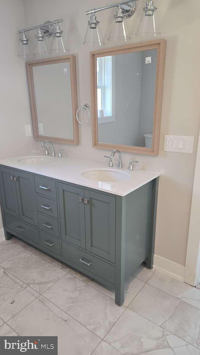 full bath featuring double vanity, marble finish floor, and a sink
