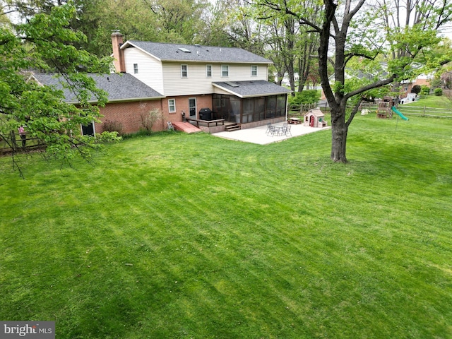rear view of house with a chimney, a sunroom, brick siding, a patio area, and a yard