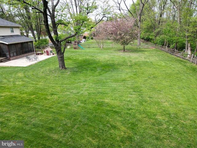 view of yard with a playground, a patio, a sunroom, and a fenced backyard