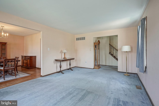 carpeted living area with baseboards, visible vents, a notable chandelier, and stairs
