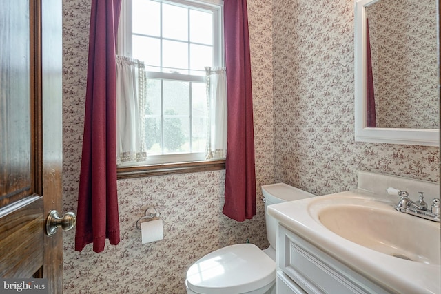 bathroom with wallpapered walls, toilet, and vanity