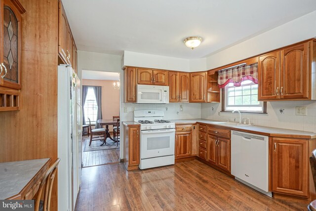 kitchen with white appliances, decorative backsplash, brown cabinetry, dark wood-style flooring, and a sink