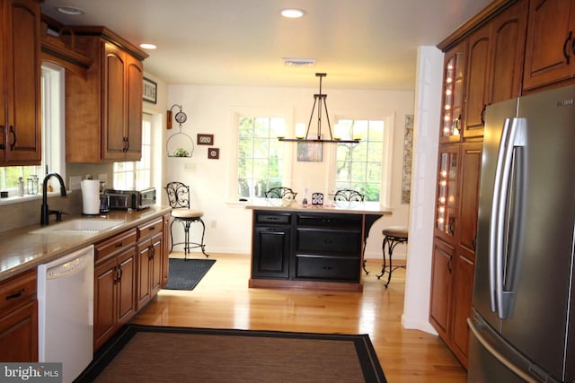 kitchen featuring a sink, white dishwasher, light wood-style flooring, freestanding refrigerator, and plenty of natural light
