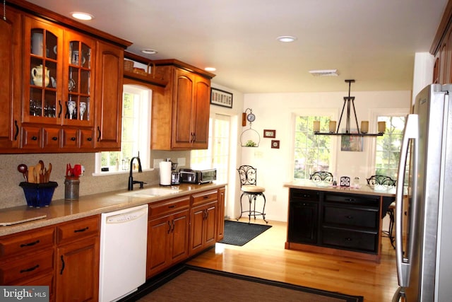 kitchen with glass insert cabinets, a sink, freestanding refrigerator, white dishwasher, and wood finished floors