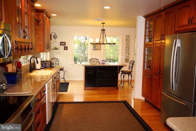 kitchen featuring light wood-style flooring, stainless steel appliances, a sink, pendant lighting, and a notable chandelier