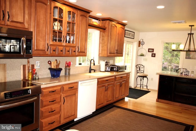 kitchen featuring brown cabinets, a sink, stainless steel appliances, dark wood-type flooring, and backsplash