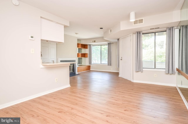 unfurnished living room with wood finished floors, baseboards, and a fireplace with flush hearth