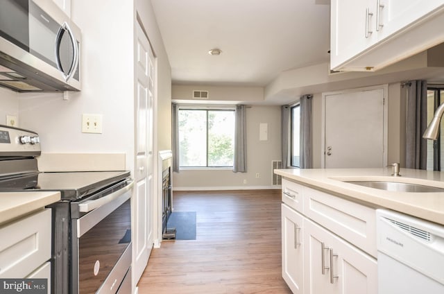 kitchen with appliances with stainless steel finishes, a sink, light wood finished floors, baseboards, and white cabinetry