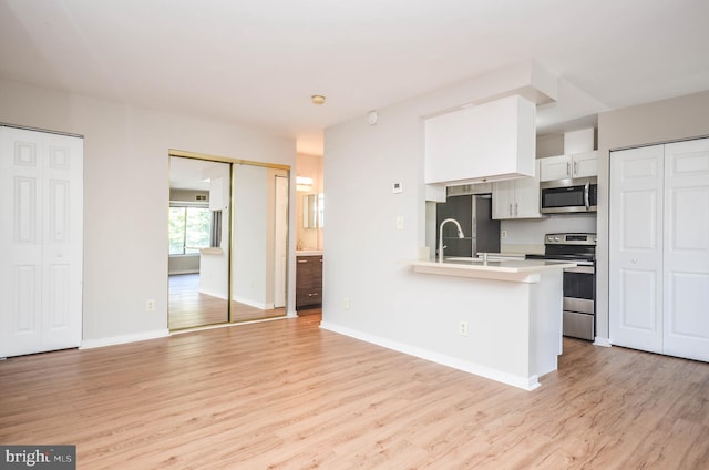 kitchen with appliances with stainless steel finishes, light wood-style flooring, light countertops, white cabinets, and baseboards