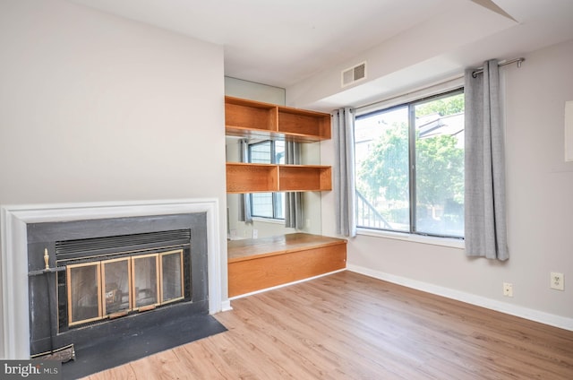 unfurnished living room featuring wood finished floors, a fireplace with flush hearth, and baseboards