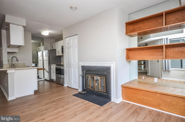 kitchen featuring stainless steel appliances, white cabinetry, light countertops, light wood-type flooring, and a fireplace with flush hearth