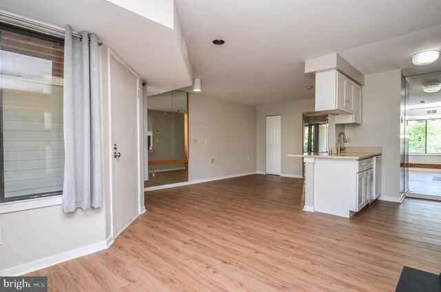 kitchen with light wood finished floors, white cabinets, light countertops, baseboards, and a sink
