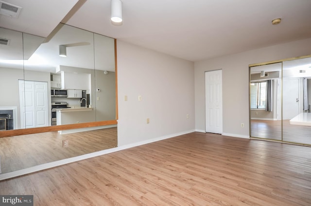 unfurnished living room with light wood-style floors, baseboards, a sink, and a glass covered fireplace