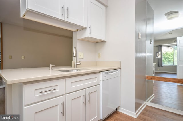 kitchen with white dishwasher, a sink, light wood finished floors, and baseboards