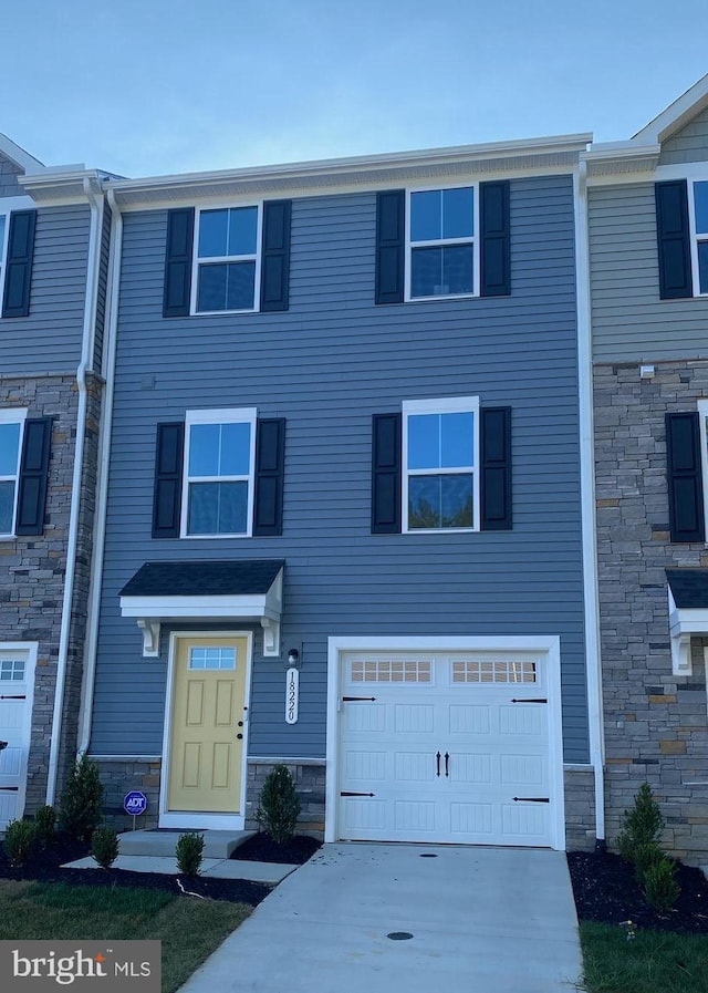 townhome / multi-family property with driveway, stone siding, and a garage
