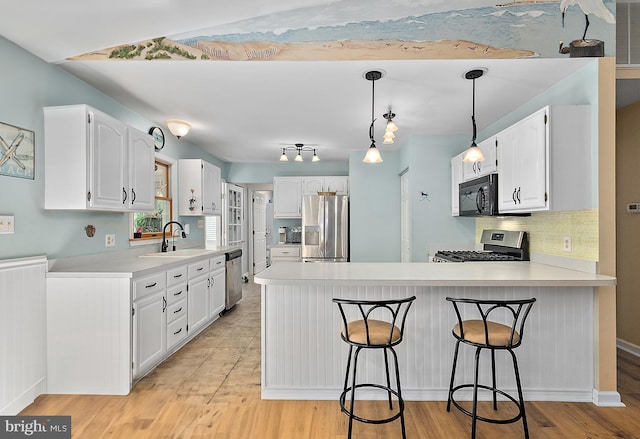 kitchen with a sink, a peninsula, white cabinets, and stainless steel appliances